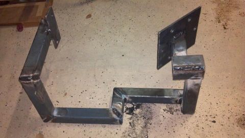 1978 Ford Bronco - Two custom-fabricated metal brackets are shown on a concrete floor, likely for automotive use.