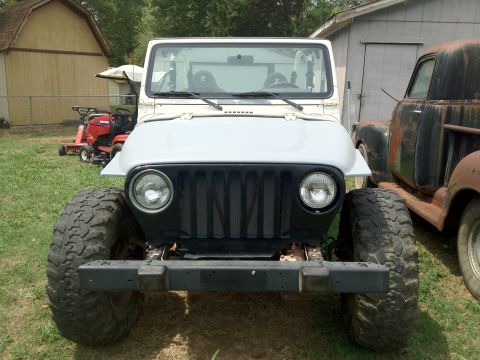 2000 Jeep TJ - A white Jeep Wrangler is parked in a yard next to an older, rusty truck, with lawnmowers in the background.