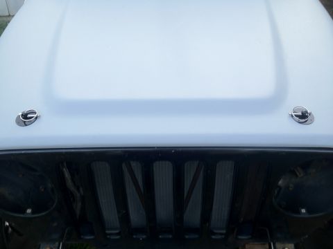 2000 Jeep TJ - The front grille and hood of a Jeep are visible, with hood pins securing the hood.