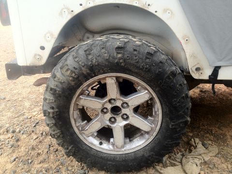 2000 Jeep Wrangler - A close-up view of a off-road tire and wheel assembly, showing significant mud and wear.