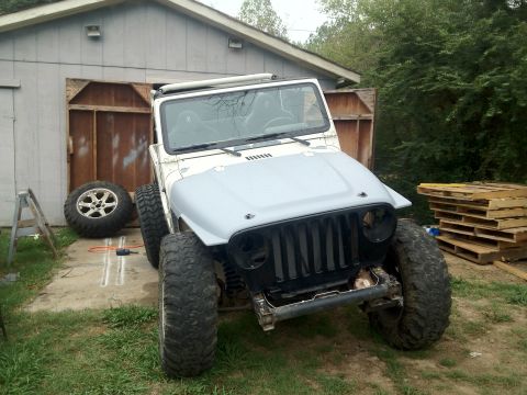 2000 Jeep TJ - A white Jeep TJ with a grey hood and black grille sits in front of a garage, with a spare tire and tools on the ground.