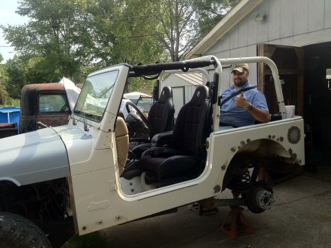 2000 Jeep TJ - A man gives a thumbs up from inside a white 2000 Jeep TJ undergoing bodywork, with one wheel removed.