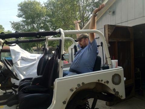 2000 Jeep TJ - A man sits in the driver's seat of a white Jeep with his arms up in the air.