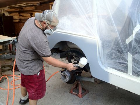 2000 Jeep TJ - A person is spray painting the fender of a vehicle that is covered in plastic sheeting.