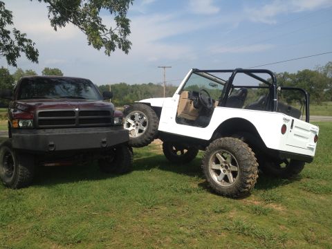 2000 Jeep Wrangler - A white Jeep Wrangler and a maroon Dodge Ram pickup truck are parked side-by-side on a grassy area under a partly cloudy sky.