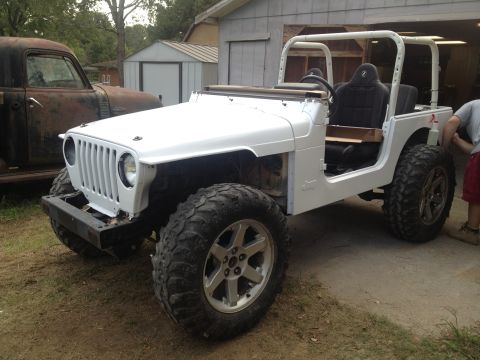 2000 Jeep TJ - A white Jeep TJ is parked outside a garage, with a rusty pickup truck to its left.
