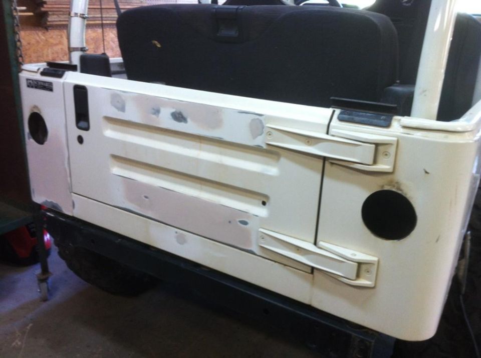 White Jeep tailgate with body filler and primer, showing two circular cutouts and side hinges