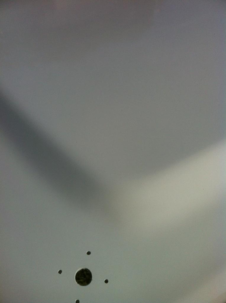 Close-up of a gray, textured surface with several small holes and one larger circular opening. A shadow falls across the upper left
