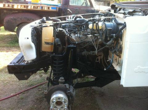 2000 Jeep TJ - The front end of a Jeep is shown with its engine and suspension components exposed, alongside an older pickup truck.