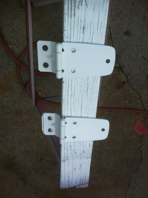 2000 Jeep TJ - Two white door hinges are mounted on a weathered wooden post, with a red hose visible in the background.