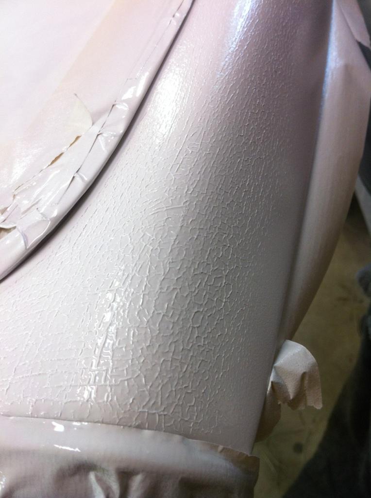 Close-up of cracked beige paint on a car interior panel, with tape visible