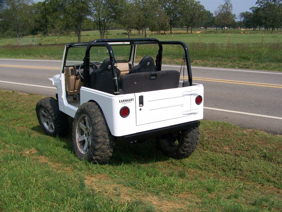 White Jeep with custom wheels and tires, rear view. 'EARNHART' text visible