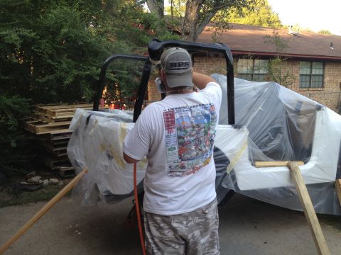 2000 Jeep TJ - Vehicle body being spray painted outdoors, with a roll cage visible.