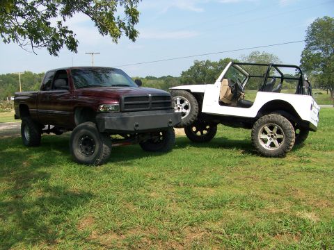 2000 Jeep Wrangler - Two modified vehicles, a pickup truck and a Jeep, are parked side-by-side in a grassy outdoor area.
