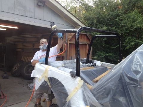 2000 Jeep TJ - A person sprays paint onto a Jeep TJ's roll cage, which is covered in protective plastic.