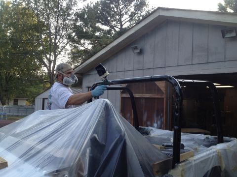 2000 Jeep TJ - A person in a mask and gloves sprays a black roll cage with a spray gun.
