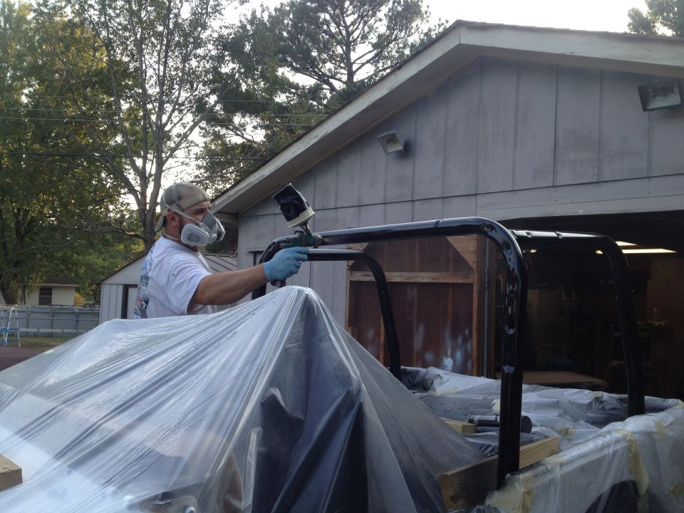Man painting black roll cage with spray gun
