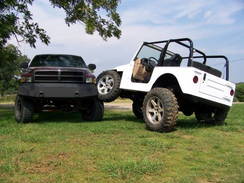 2000 Jeep Wrangler - Two modified off-road vehicles, a white Jeep and a maroon Dodge Ram, are parked on a grassy field.