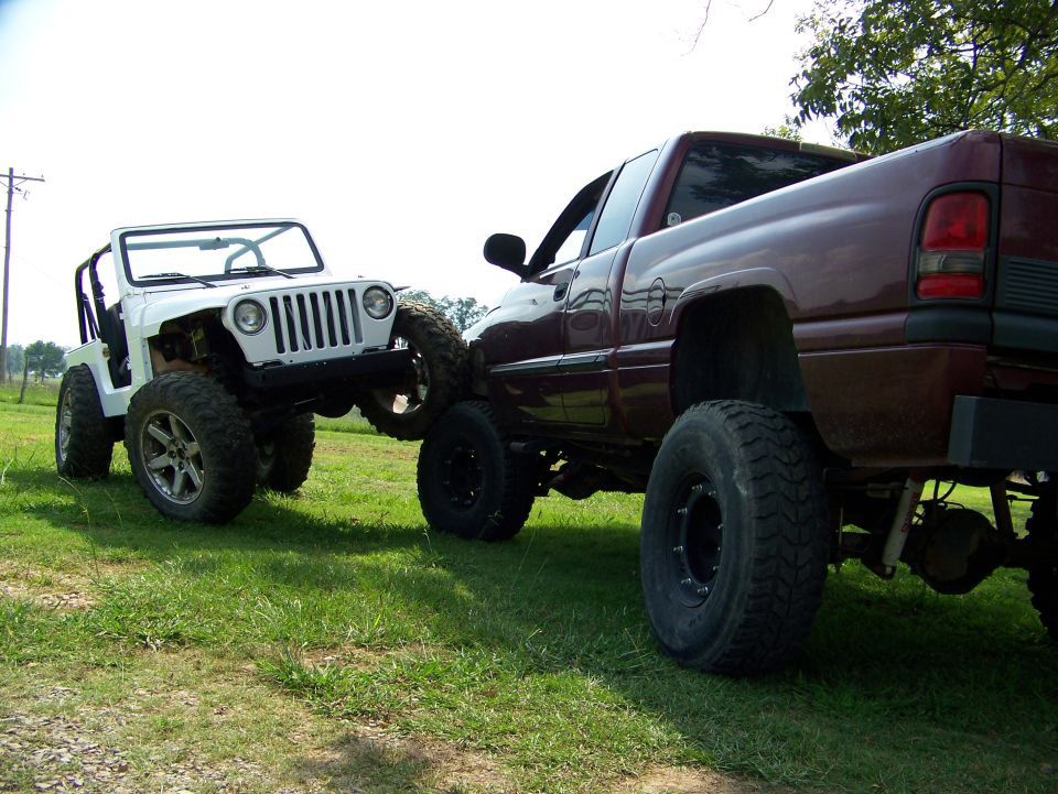 White Jeep TJ being towed by a maroon Dodge Ram pickup truck, both lifted
