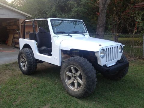 2000 Jeep TJ - This modified Jeep Wrangler features large off-road tires and custom wheels, sitting in a grassy yard.