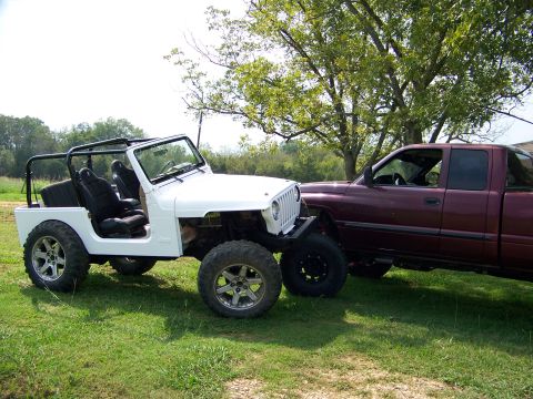 2000 Jeep Wrangler - A white Jeep Wrangler is parked next to a maroon pickup truck on a grassy area under trees.