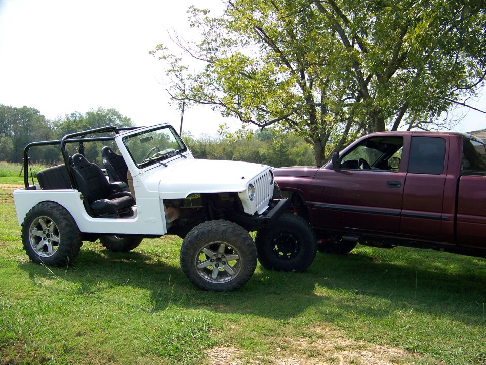 White Jeep Wrangler with aftermarket wheels and roll cage parked next to a maroon pickup truck