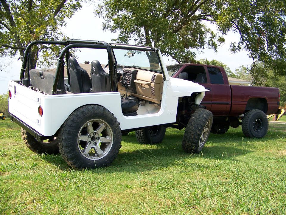 White Jeep Wrangler parked next to a red pickup truck on grass