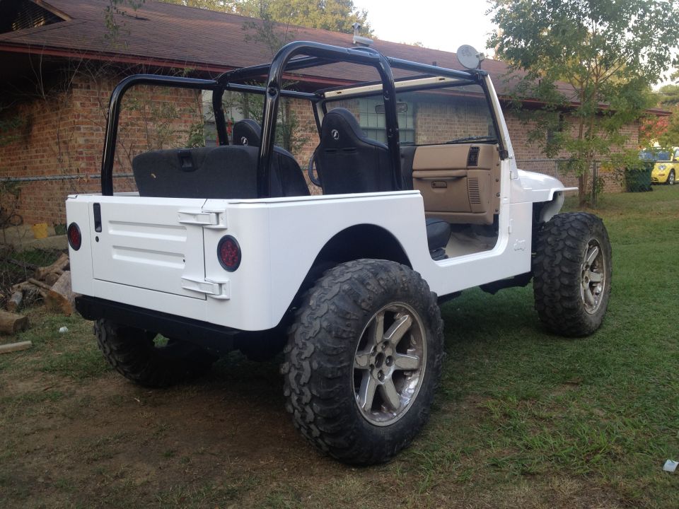 White Jeep TJ with aftermarket wheels and roll cage, parked on grass