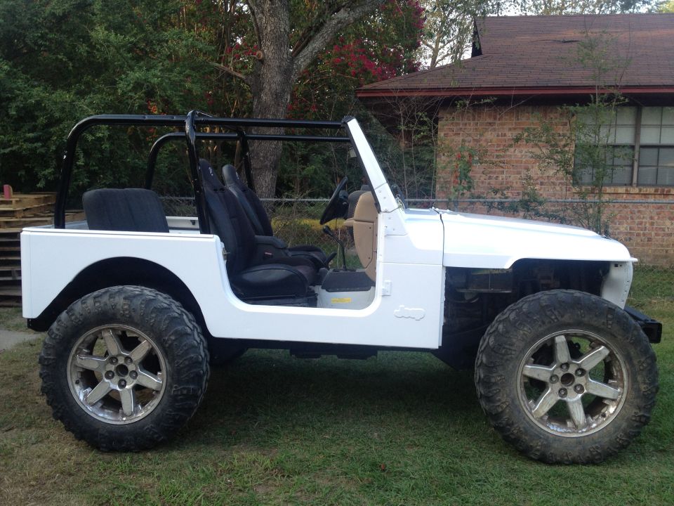 White Jeep with black roll cage and aftermarket wheels, side view