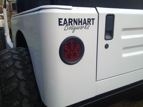 2000 Jeep TJ - Close-up of a white Jeep's rear, showing a custom body shop decal and a circular LED taillight.