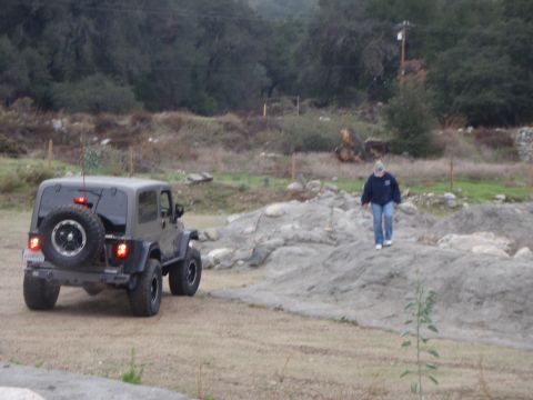 1978 Ford Bronco - A dark gray Jeep Wrangler is viewed from the rear, parked on a dirt road with a person walking on a rocky incline in the background.