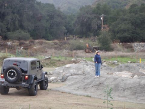 1978 Ford Bronco - A Jeep Wrangler is parked on a dirt road with a woman standing on a rocky incline in the background.