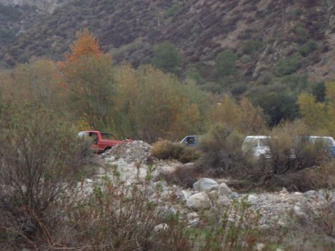 1978 Ford Bronco - Several vehicles are parked in a dry riverbed surrounded by brush and hills.