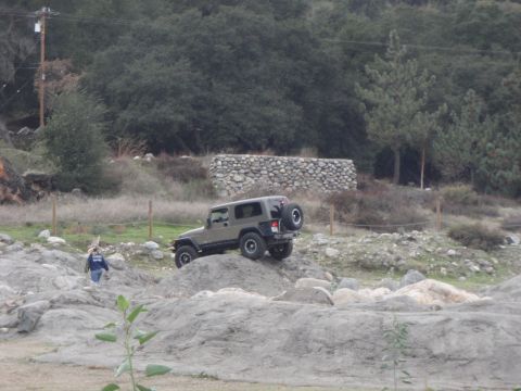 1978 Ford Bronco - A Jeep Wrangler navigates a challenging off-road course with a stone wall in the background.