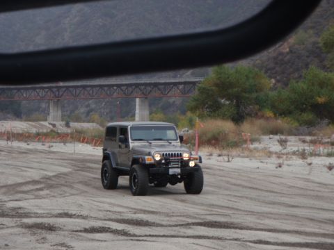 1978 Ford Bronco - A Jeep Wrangler navigates a sandy terrain under a large bridge structure.