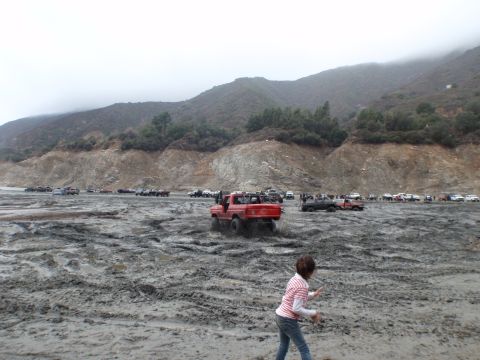 1978 Ford Bronco - Multiple off-road vehicles navigate a muddy terrain under overcast skies.
