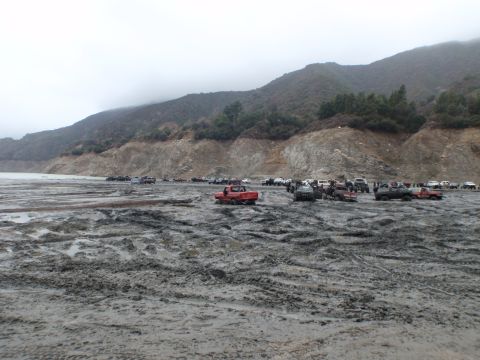 1978 Ford Bronco - A large gathering of off-road vehicles navigates a challenging muddy landscape under an overcast sky.