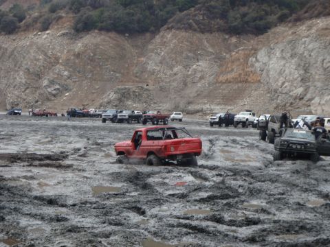 1978 Ford Bronco - A red 1978 Ford Bronco is stuck in a muddy off-road area with other vehicles present.