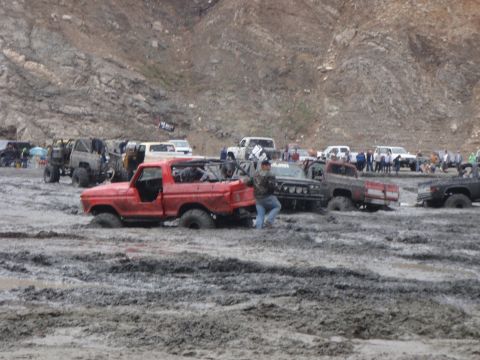 1978 Ford Bronco - Multiple off-road vehicles are mired in mud during an event, with a red 1978 Ford Bronco prominently stuck.