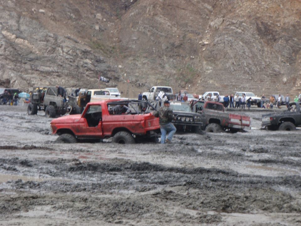 Red 1978 Ford Bronco with its top removed, stuck in thick mud, viewed from the front-right