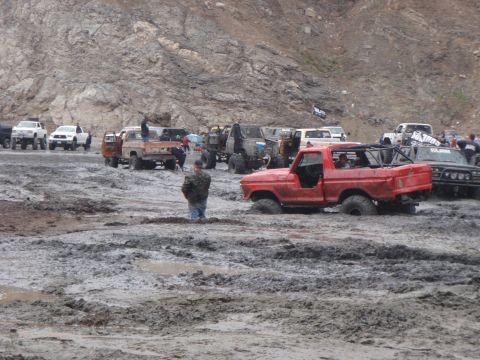 1978 Ford Bronco - Multiple off-road vehicles navigate a muddy terrain, with a red 1978 Ford Bronco prominently stuck.