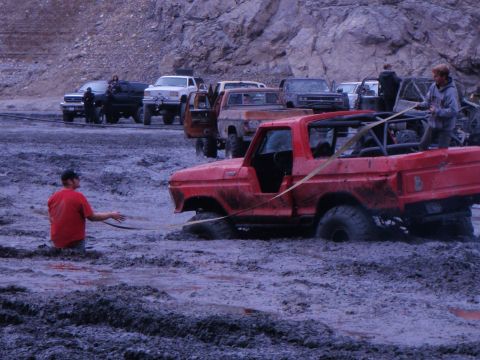 1978 Ford Bronco - A red 1978 Ford Bronco is stuck in thick mud, with a person in the foreground and other vehicles in the background.