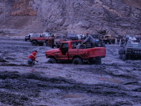 1978 Ford Bronco - Multiple off-road vehicles are stuck in thick mud, with people attempting to free a red pickup truck.
