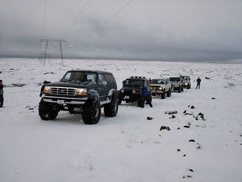 1996 Ford Bronco - A convoy of off-road vehicles, including a Ford Bronco and several Jeeps, travels through a snowy terrain.