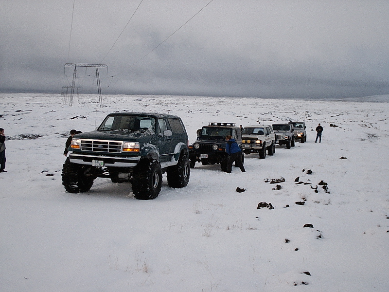 Dark green lifted Ford Bronco on big tires in snowy field with other 4x4s