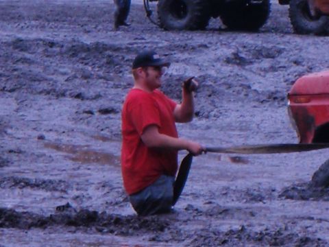 1978 Ford Bronco - A man is stuck in the mud while holding a tow strap, with other vehicles visible in the background.