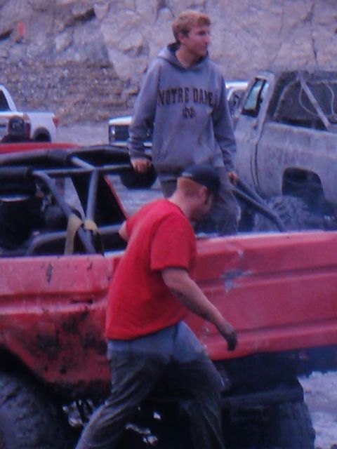 1978 Ford Bronco - Two men stand near a red off-road vehicle and a grey pickup truck in a muddy outdoor setting.