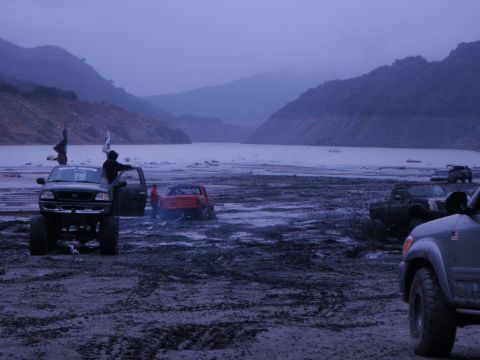 1978 Ford Bronco - Several vehicles are stuck in the mud near a body of water under a hazy sky.
