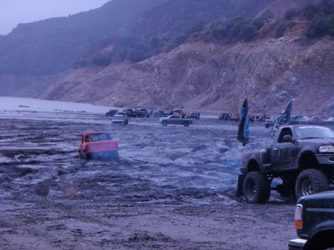 1978 Ford Bronco - Several trucks and SUVs are parked and driving in a muddy, dry lake bed with a mountain in the background.
