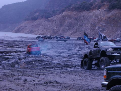 1978 Ford Bronco - Multiple trucks gathered in a muddy off-road area, with one vehicle stuck and another prominently displayed.